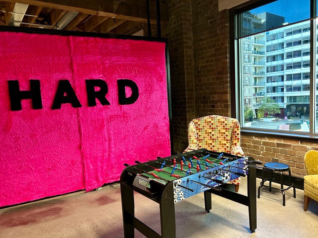 Table soccer in a student space with a hot pink wall hanging and the word 'hard'